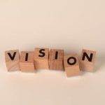 Wooden blocks with black letters spelling 'VISION' on a light beige background, symbolizing foresight and goals.